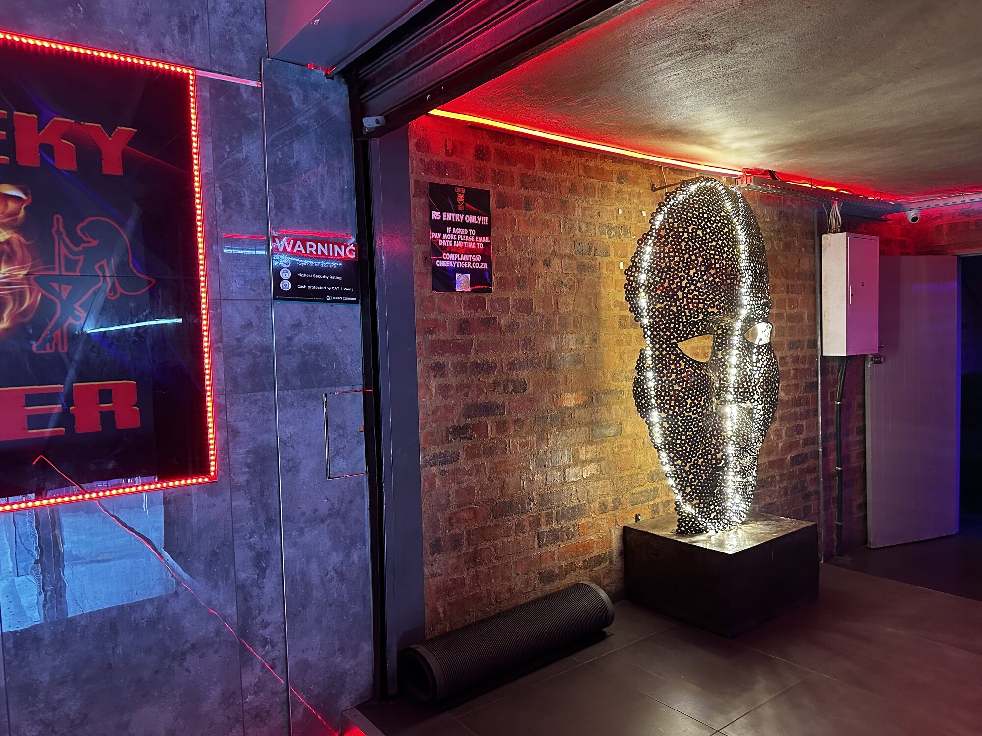 Entrance passage with the steel mask sculpture and neon Cheeky Tiger sign at Midrand