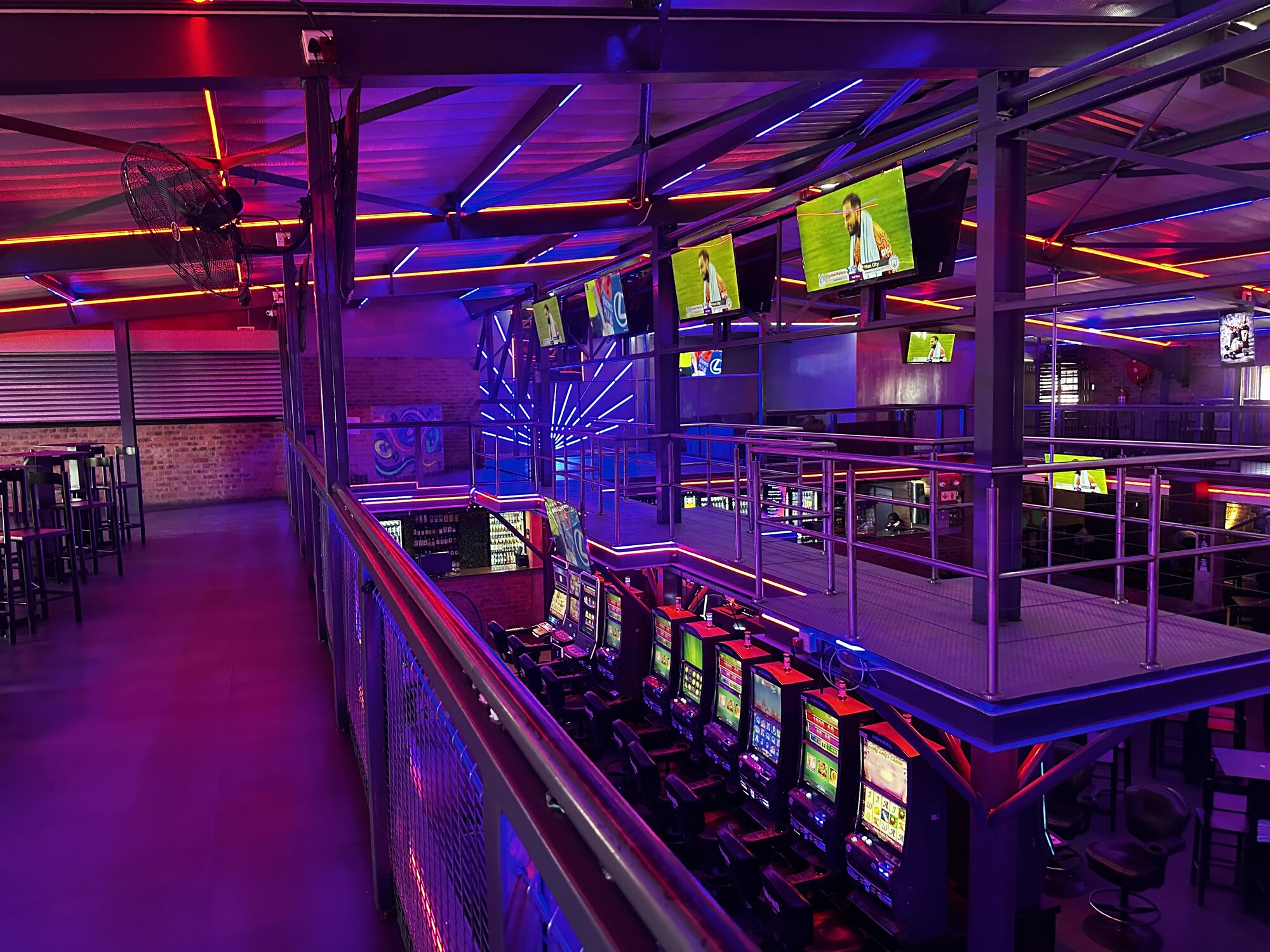 Slot machines lining the mezzanine walkway below the sports screens at Cheeky Tiger Midrand