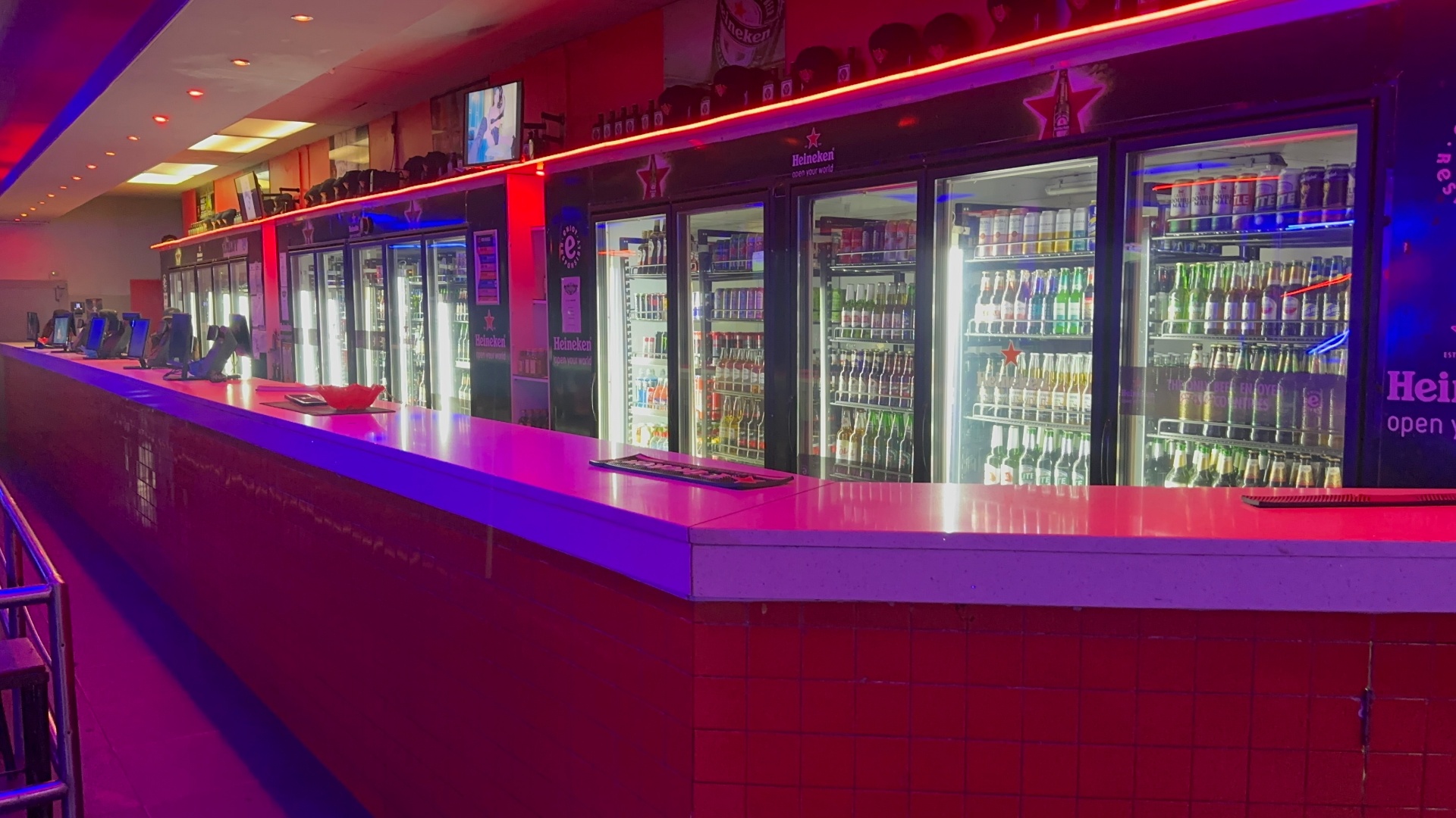Long main bar with fully stocked fridges under red and blue neon at Cheeky Tiger Kempton Park