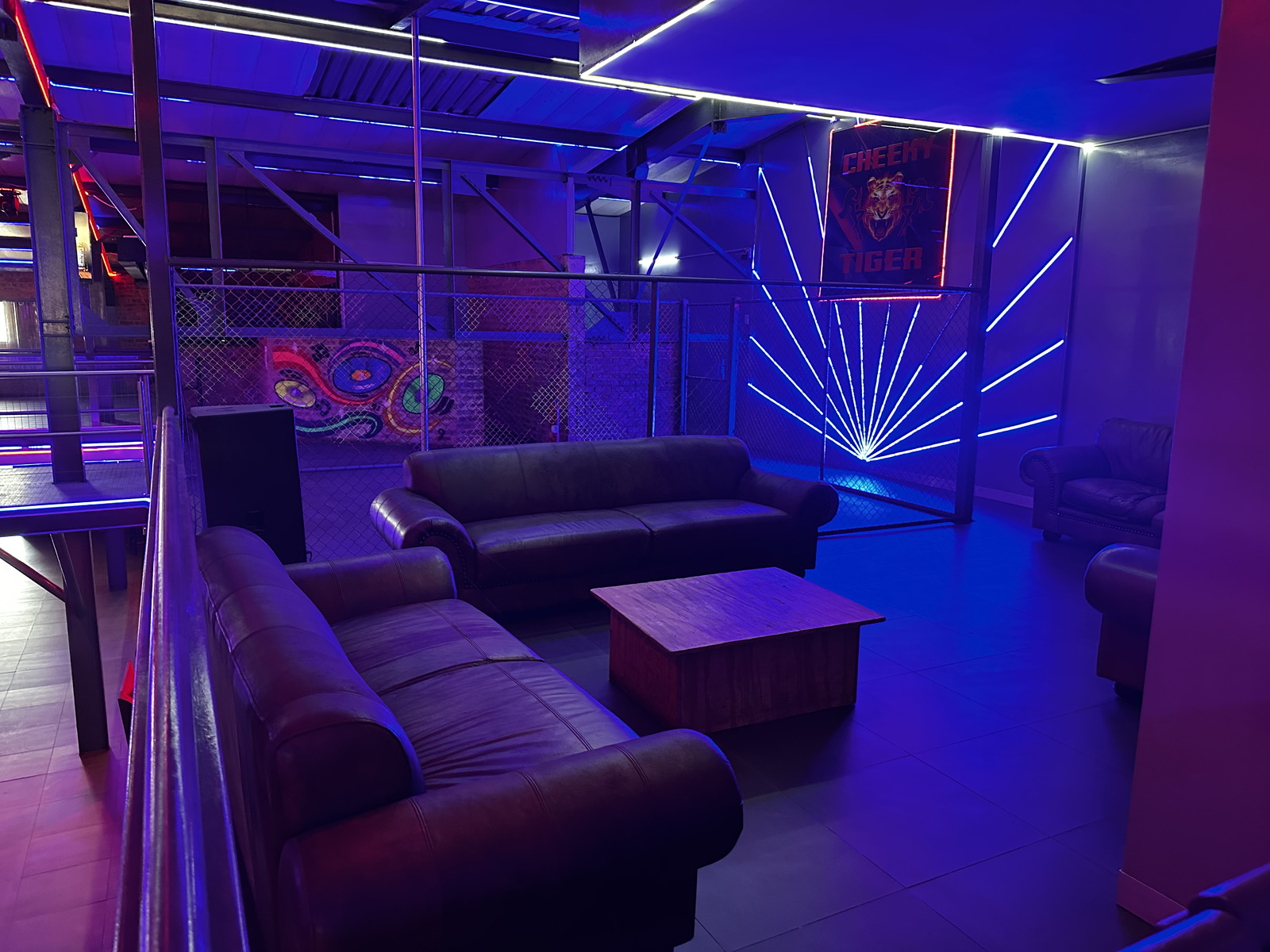 VIP leather lounge seating beside the blue neon sunburst wall at Cheeky Tiger Midrand